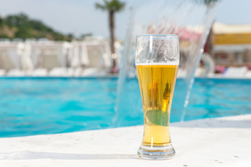 Glass of ice cold beer at the edge of a pool