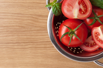 Tomatoes with basil in colander on wooden table background. Food composition. Top view