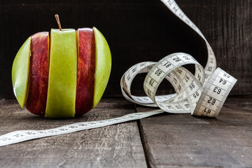  apple surrounded by a measuring tape referring to diet and health concept on wooden background