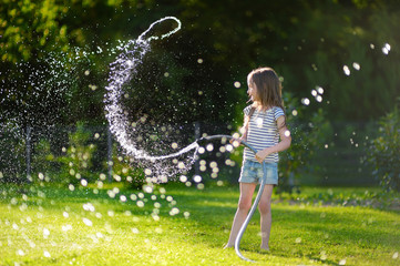 Adorable little girl playing with a garden hose