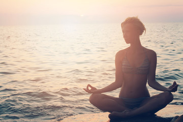 Fototapeta na wymiar Yoga woman meditating in lotus pose on the beach during sunset