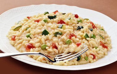 Dish of risotto zucchini peas tomatoes with fork