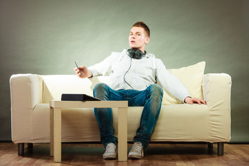man on couch with headphones smartphone and tablet