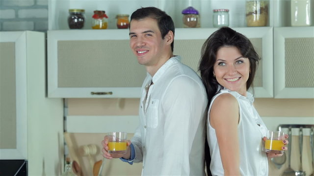 Newly married couple standing back to back holding orange juice