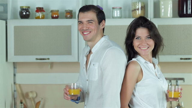 Couple standing back to back holding orange juice