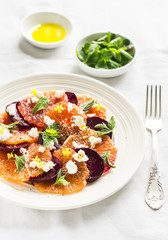 fresh salad with oranges, beets and feta cheese on a white plate on a light  surface