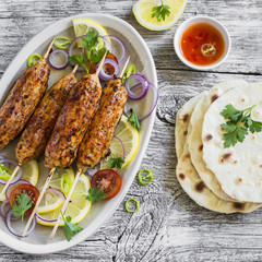 chicken kebabs on wooden skewers on an oval plate and homemade tortilla on a light wooden surface