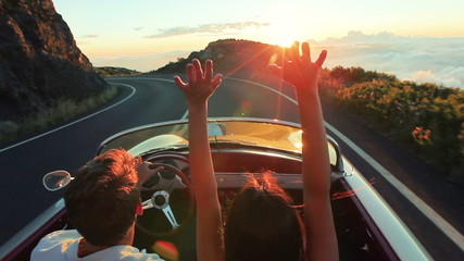 Couple driving convertible car. steadicam shot with flare into sunset in Hawaii