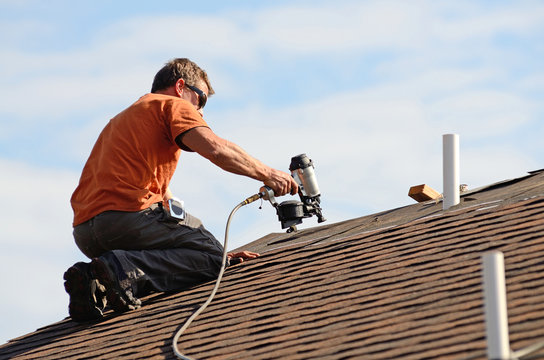 Building contractor putting the asphalt roofing on a large commercial apartment building.