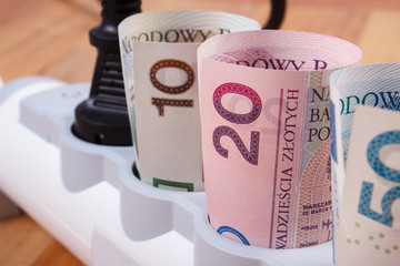 Rolls of polish currency money in electrical power strip with connected plug, energy costs