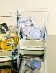one glass of whiskey and one empty with ice cubes on table with reflection