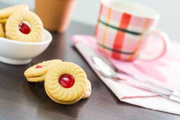 Sandwich cookies with cream and strawberry flavoured jam on wood