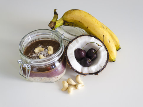 Cherry Coconut Banana Overnight Oats With Cracked Open Coco,banana,cashews Mixed With Chia Seeds,cherry Cream In A Mason Jar,tropical Meal Top View Wooden Background.Healthy Fitness Breakfast Oatmeal