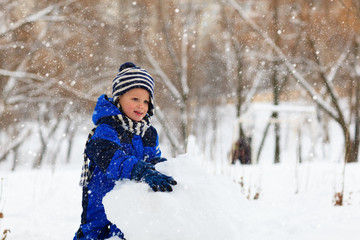 Fototapeta na wymiar little boy building snowman in winter park