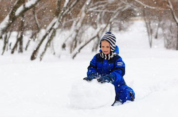 Fototapeta na wymiar little boy building snowman in winter park