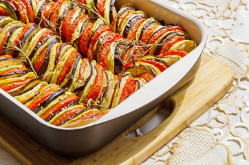 freshly baked mixture of satay and ratatouille in a cooking form on a wooden board on an ornamental...