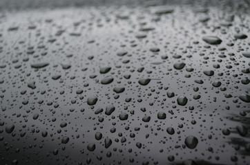 Water droplets on a very dark green, shiny, painted metal surface