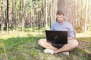 young man working with his laptop outdoors in nature