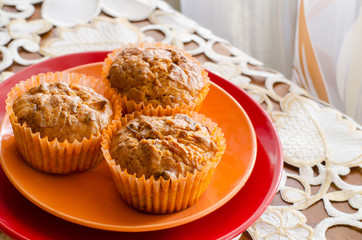 close-up of three lemon muffins on an orange and red plate on a white decorated table cloth 