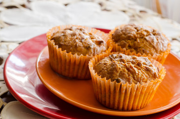three lemon muffins on an orange and red plate on a white decorated table cloth 