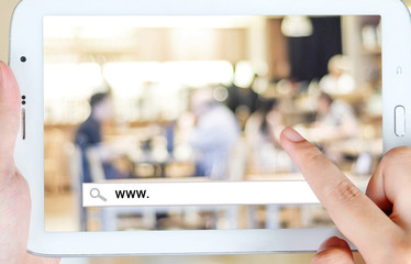 Hand holding tablet with www. word on search bar over blur resta