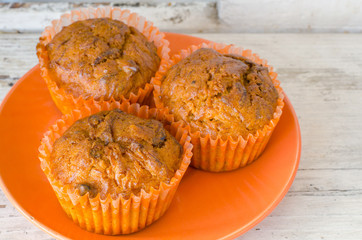 close-up of an orange plate with three lemon muffins on an old white wooden surface 