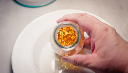 Man hand hold bottle to show fish oil pills  on white plate vint
