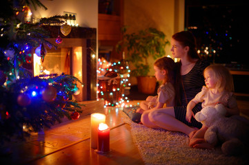 Young mother and daughters sitting by a fireplace on Christmas