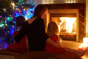 Obraz na płótnie Canvas Young mother and daughters sitting by a fireplace on Christmas