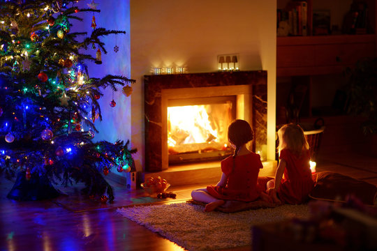 Happy little girls sitting by a fireplace on Christmas eve