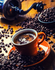 Coffee. Cup of black coffee spilled coffee beans and grinder in the background 