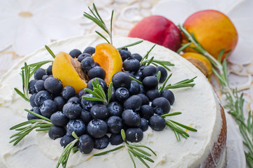 close-up of delicious home made layered cake with cream, berries, rosemary and nectarine on top on a decorative white table cloth
