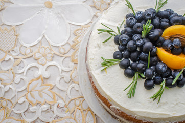 top view of delicious home made layered cake with cream, berries, rosemary and nectarine on top on a decorative white table cloth