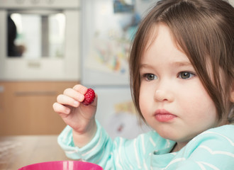 A cute little girl holding a raspberry