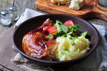 glazed roasted chicken leg with mashed potatoes and vegetable salad on a wooden background
