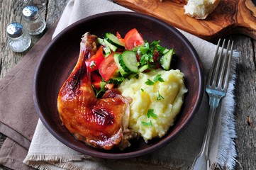 glazed roasted chicken leg with mashed potatoes and vegetable salad on a wooden background