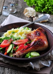 glazed roasted chicken leg with mashed potatoes and vegetable salad on a wooden background
