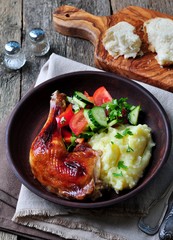 glazed roasted chicken leg with mashed potatoes and vegetable salad on a wooden background