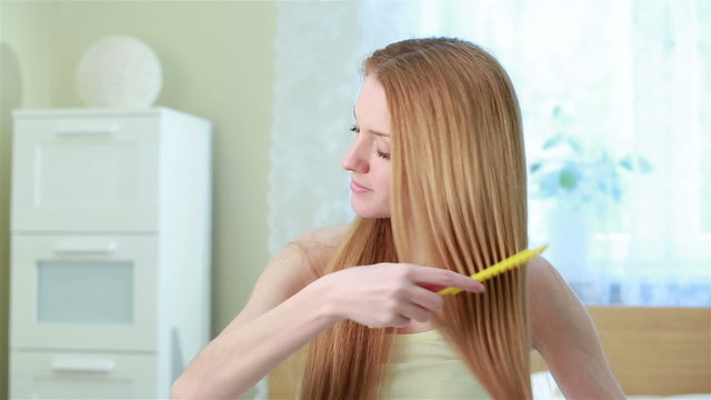 Charming young red-haired woman combing her long hair and smiling.