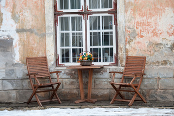 Fototapeta na wymiar Table and two wooden chairs on the pavement in Tallinn Old Town Estonia. Snow can be seen on the pavement.