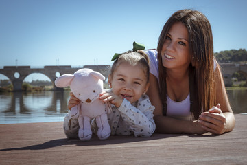Madre e hija acostadas en el embarcadero. Una niña y su mama disfrutando del verano junto al rio. Madre joven soltera.