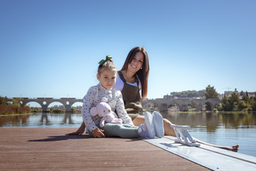 Madre e hija sentadas en el embarcadero. Una niña y su mama disfrutando del verano junto al rio. Madre joven soltera.