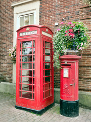 Traditional British red phone box andletterbox in pretty street with flowers.