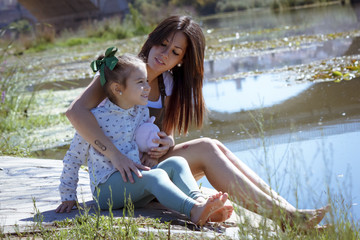 Madre e hija sentadas en el embarcadero. Una niña y su mama disfrutando del verano junto al rio....