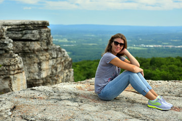 Fototapeta na wymiar Young woman sitting at the edge of roc at Minnewaska State Park Reserve Upstate NY during summer time