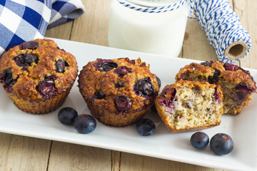 Homemade muffin on a wooden table with fresh berries and blue decoration around it.