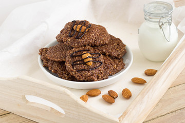 Homemade gluten-free and sugar-free almond cookies with cocoa and chocolate sauce on a wooden tray.