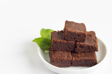 Homemade chocolate brownies with mint leaves on a white plate, white background.
