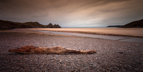 Driftwood and pebbles at Three Cliffs Bay on The Gower peninsular, South Wales.