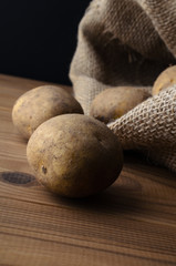 Potatoes Spilling from Sack on to Wood Plank Table